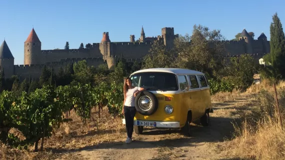 Emilie Broussouloux avec un combi avec des vignes autour et la cité de Carcassonne en fond